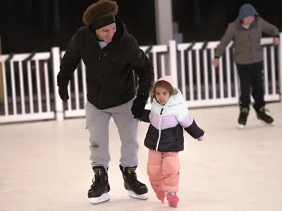 Father and young daughter ice skating on the township's artificial ice rink