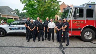 Meridian Township police and firefighters posing in front of a police car and firetruck